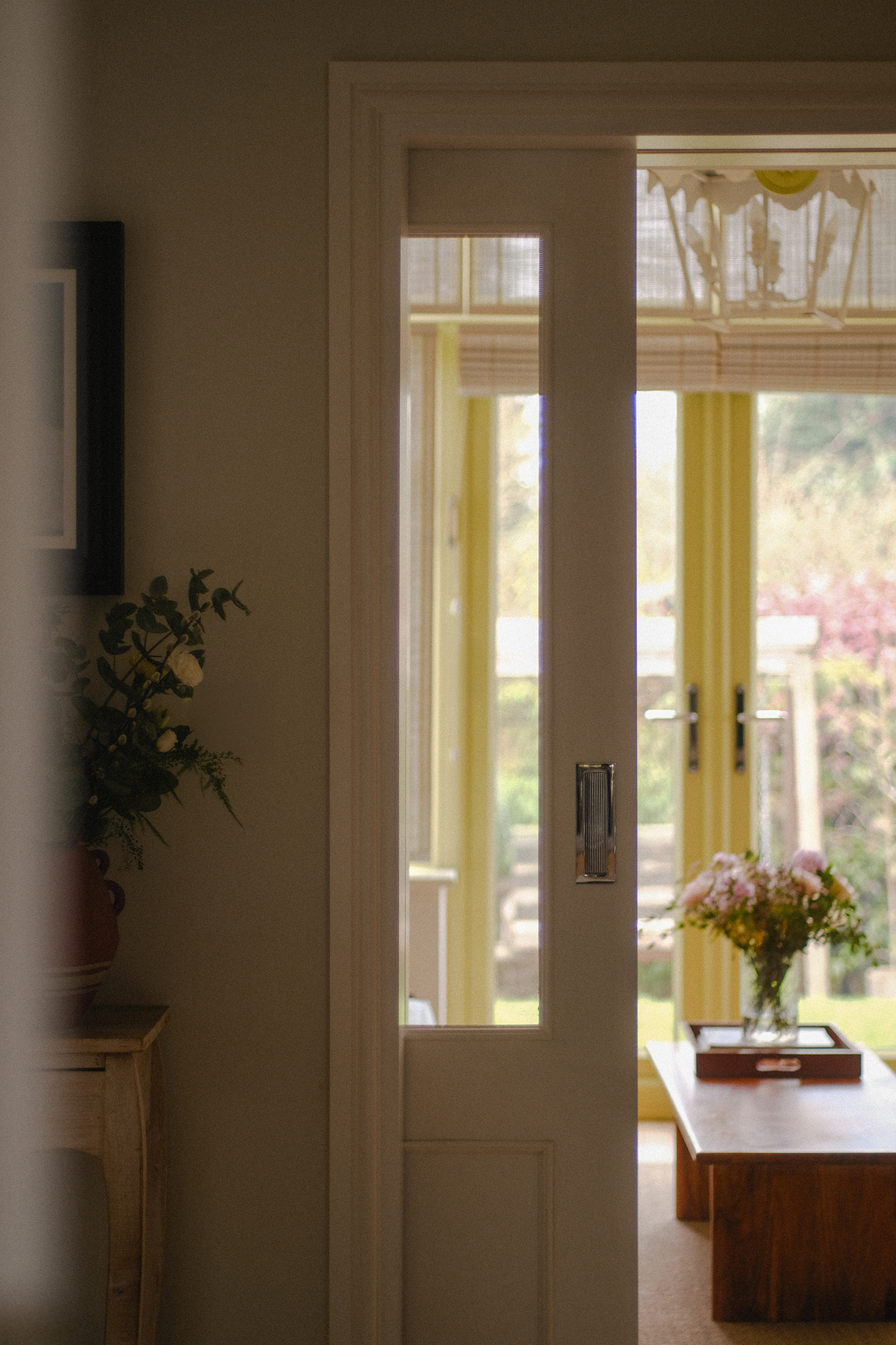 View through a sliding pocket door into the garden room, with glazed doors and a timber coffee table beyond.
