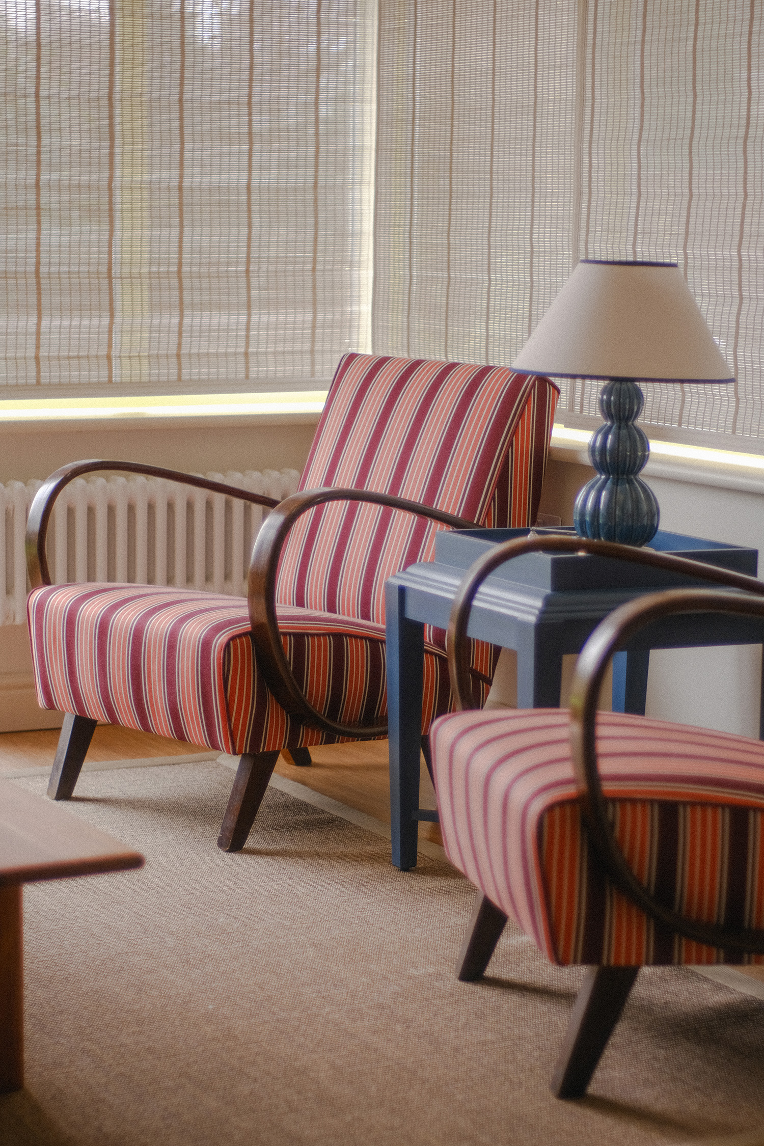 Blue ceramic table lamp on a painted side table beside a striped upholstered armchair.