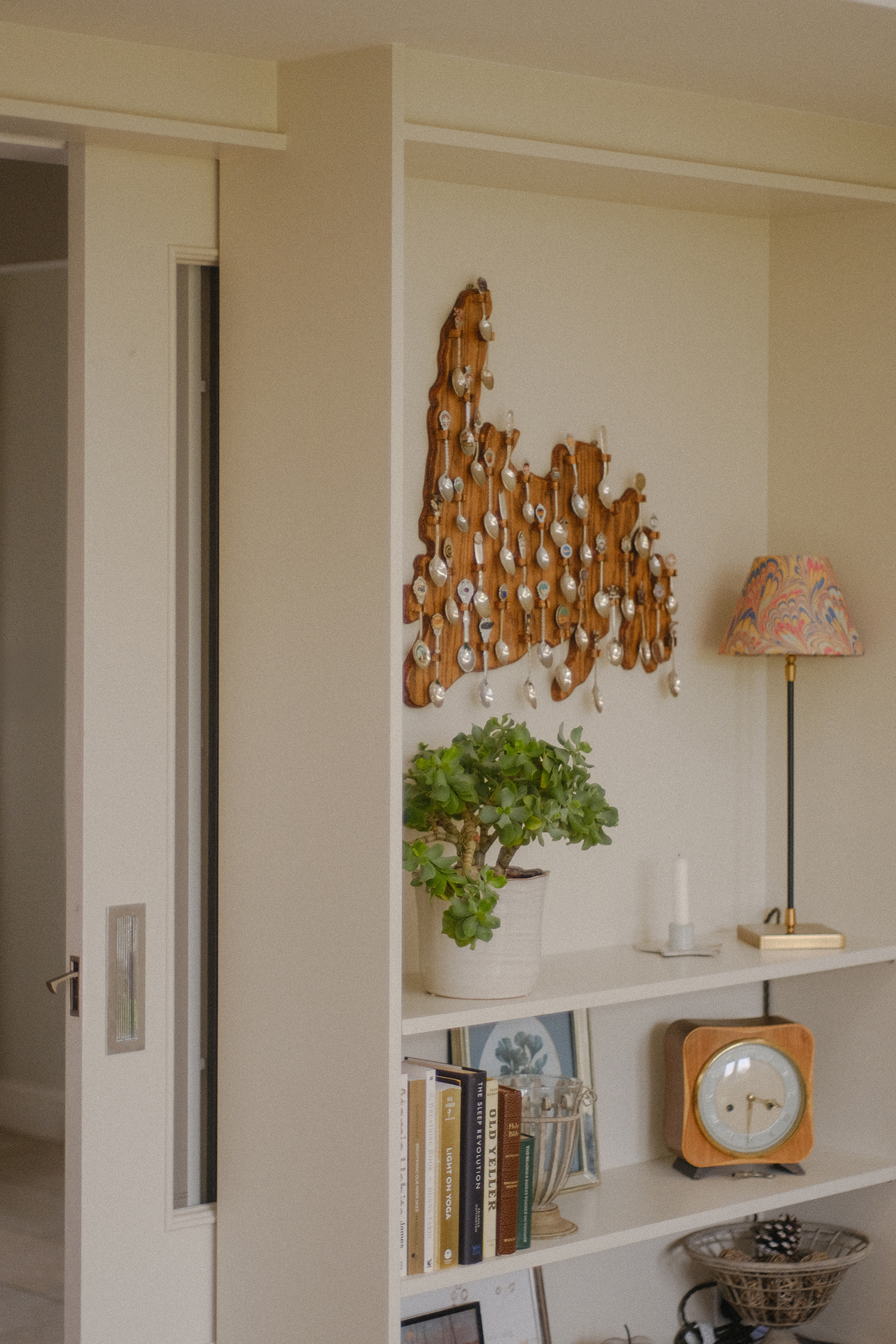 Built-in display shelves with books, a small clock and plant beneath decorative wall art in a neutral interior