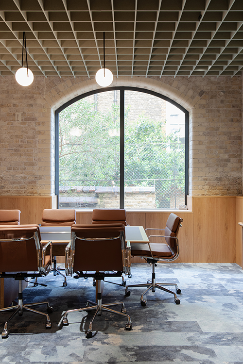 Boardroom with arched window, exposed brick walls, bespoke oak joinery and contemporary meeting furniture.