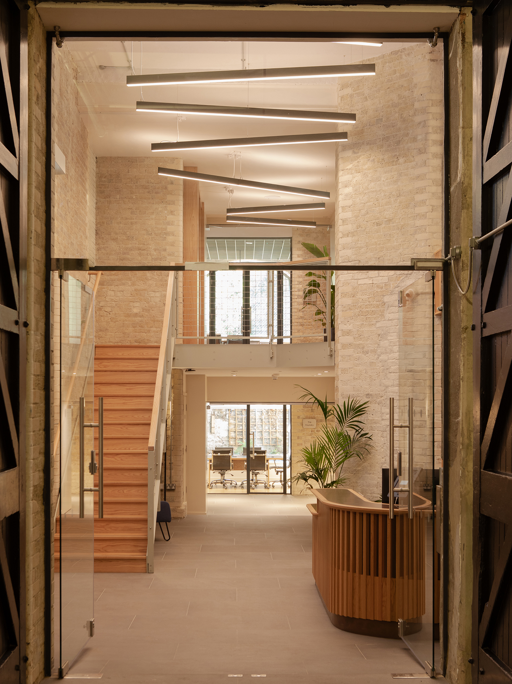 Reception space within a Clerkenwell workplace retrofit featuring exposed brickwork, bespoke timber reception desk, new staircase and retained industrial structure.
