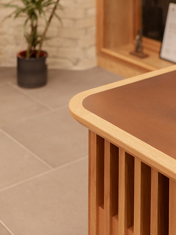 Curved timber reception desk with vertical oak slats and integrated work surface within the reception atrium.