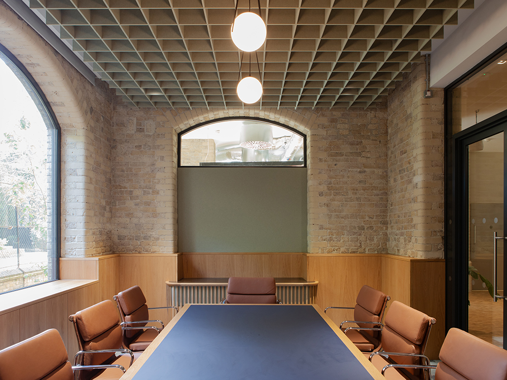 Meeting room featuring exposed brickwork, bespoke joinery, gridded ceiling installation and large meeting table.
