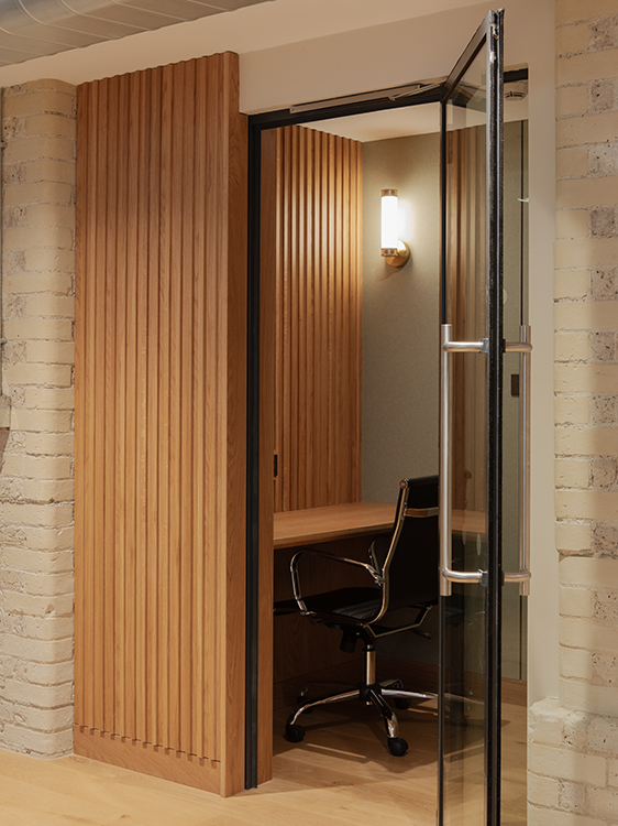 Private meeting booth clad in vertical timber slats with integrated desk, lighting and glazed entrance.