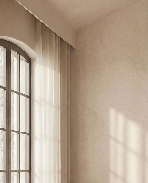 Arched steel-framed window with sheer linen curtains filtering natural light into the bedroom.