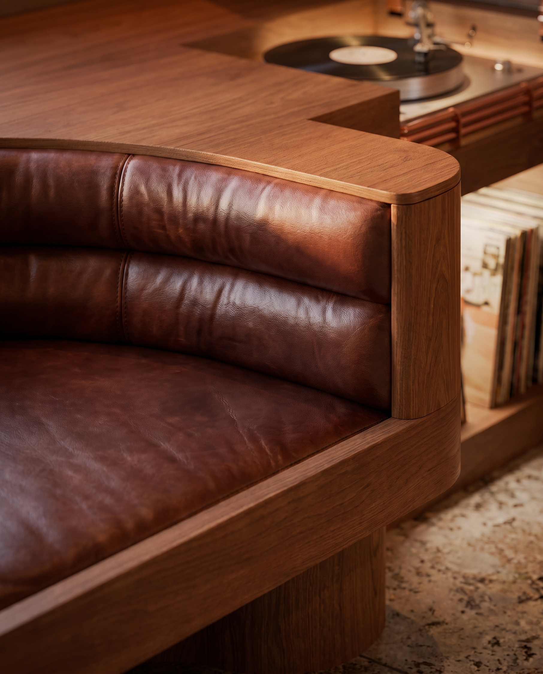 Curved timber seating with deep brown leather upholstery beside a turntable and vinyl records