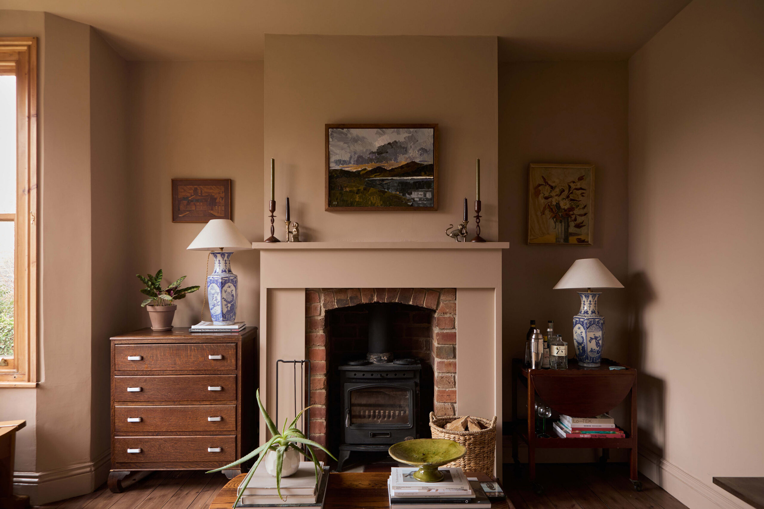 Living room with restored brick fireplace, warm clay-toned walls, original timber floorboards and collected vintage furnishings.